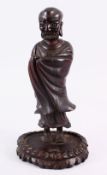 A 19TH CENTURY CHINESE CARVED HARDWOOD FIGURE OF A LUOHAN, stood wrapped in his gowns, upon a carved