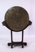 A LARGE CHINESE CIRCULAR CAST BRONZE 'MIRROR' on a hardwood stand (stand AF), disc 46cm diameter.