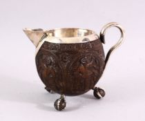 A FINELY CARVED THAI COCONUT JUG WITH SILVER MOUNTS, on three ball feet, 10cm high .