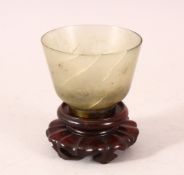 A GOOD JADE CUP on a wooden stand. 2.5ins diameter.