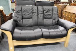 A Stressless beech framed and black leather upholstered two seater reclining settee.