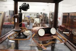 A candlestick telephone and a cased pair of binoculars.