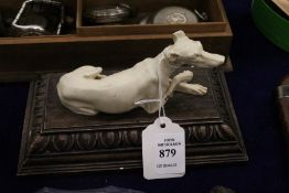 A model of a greyhound reclining on a carved wood base.
