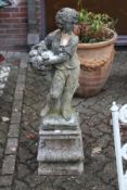 A composite garden figure of a young boy holding a basket of flowers on a pedestal base.