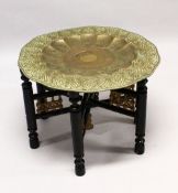 A GOOD LARGE ISLAMIC BRASS TRAY TABLE AND FOLDING STAND, with embossed decoration, 76cm diameter.