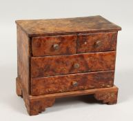 A SMALL MINIATURE THUYA WOOD FOUR DRAWER CHEST on bracket feet. 7ins wide.