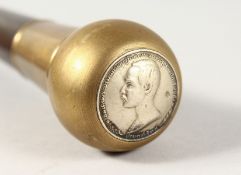 A WALKING CANE with BRASS HANDLE inset with a coin. 2ft 11ins long.