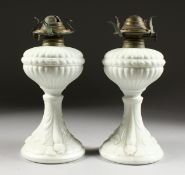 A PAIR OF WHITE OPALINE OIL LAMPS with dolphin supports on circular bases. 9ins high.