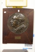 A cast bronze circular portrait plaque mounted on a mahogany backing board.