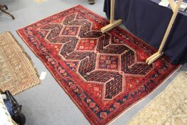 A Persian rug, red ground with three large diamond shaped central motifs.