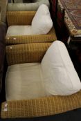 A pair of large wicker conservatory armchairs with loose cushions.