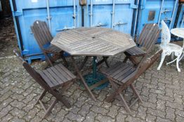A hardwood folding garden table with four chairs and a parasol stand.