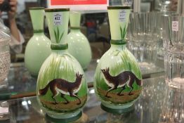 A pair of green opaque glass vases painted with foxes in a landscape.
