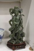 A Chinese carved jadeite figure of Guanyin on a wooden base.