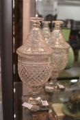 A pair of late 19th century / early 20th century cut glass pedestal urns and covers on square