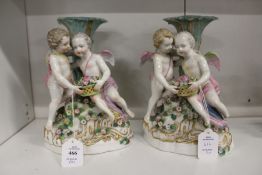 A pair of 19th century porcelain figural candlesticks, each with a pair of cherubs holding a