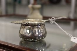 A silver tea strainer and stand.