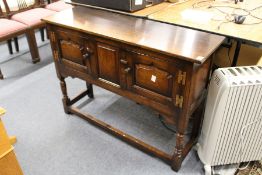 An oak sideboard with two panelled cupboard doors on turned legs, united by stretchers.