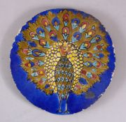 AN INDIAN CIRCULAR POTTERY TILE OF A PEACOCK, stood displaying its feathers, 20cm