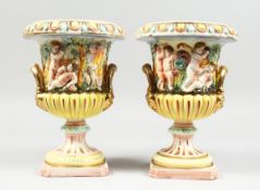 A PAIR OF CAPODIMONTE STYLE POTTERY URNS AND COVERS with panels of cupids. 9 ins. high.