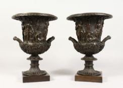 A GOOD PAIR OF CLASSICAL TWO HANDLED BRONZE URNS on square bases 12 ins high.