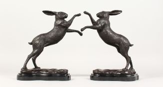 A PAIR OF BRONZE BOXING HARES on a shaped marble base 11 ins high.