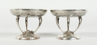 A PAIR OF HAMMERED SILVER SWEETMEAT DISHES on three curving legs and circular base. London 1925,