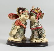 A JAPANESE STYLE POTTERY GROUP of two young children kissing, 7 in. high