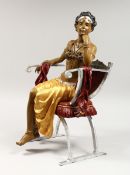 A PAINTED AND GILDED BRONZE GIRL sitiiing on a chair 16 ins high