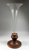 A LARGE FACETED GLASS TRUMPET-SHAPED VASE set into a circular wooden base, 2 ft. 9 in. high.