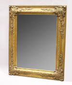 A LARGE GILT BEVELLED MIRROR with scrolling decoration, 5 ft. 3 in. high, 4 ft. 2 in. wide.