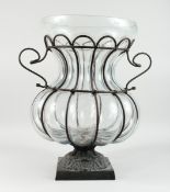 A LARGE SHAPED MOULDED GLASS BULBOUS VASE in a metal stand with square base, 20 ins high.