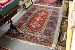 A Persian rug, red ground with large central cross shaped motifs.