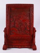 A CHINESE RELIEF CINNABAR LACQUER STYLE TABLE SCREEN & STAND, with scenes of immortal figures in