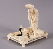 A GOOD 19TH CENTURY INDIAN CARVED IVORY GROUP OF A SNAKE CHARMER, standing charming a cobra from a