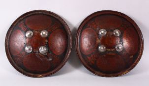 A GOOD PAIR OF INDIAN PAINTED AND LACQUERED LEATHER SHEILDS, each with four glass roundels,