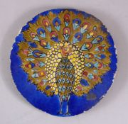 AN INDIAN CIRCULAR POTTERY TILE OF A PEACOCK, stood displaying its feathers, 20cm