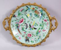 A CHINESE CELEDON CIRCULAR DISH, painted with birds and flowers in an ormolu frame with handles,