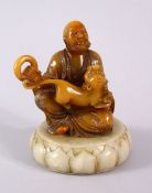A CHINESE CARVED AMBER COLOUR SOAPSTONE FIGURE OF LOUHAN - in a seated pose with a kyllin and a