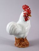 A CHINESE PORCELAIN FIGURE OF A COCKEREL, seated upon stylized wooded stump, red lacquer facial