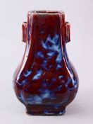 A CHINESE FLAMBE GLAZED PORCELAIN VASE, the gu shaped vase with an ox blood red ground with white