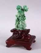 A GOOD GREEN JADITE CARVING OF FLOWERS, 13cm high, on a carved wooden stand.