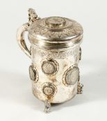 A CONTINENTAL .835 SILVER TANKARD AND COVER inset with silver coins on three lion feet. 6.5ins