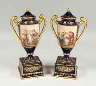 A GOOD PAIR OF VIENNA PORCELAIN TWO HANDLED URNS ON STANDS, rich blue and gilt ground painted with