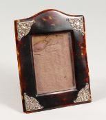 A SILVER MOUNTED UPRIGHT TORTOISESHELL PHOTOGRAPH FRAME with serpentine top and leather back, 6