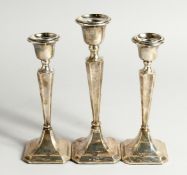 A SET OF THREE SILVER CANDLESTICKS with loaded bases. Chester 1904 & 1924 8ins and 6ins high