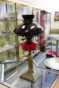 A brass oil lamp with ruby colour brass reservoir and opaque glass shade.