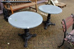 A pair of circular zinc topped tables with cast iron bases.