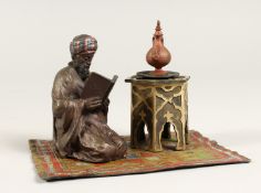 A PAINTED BRONZE OF AN ARAB, reading on a carpet. 5.5ins long.