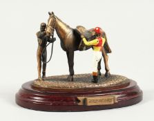 AFTER THE RACE, a painted metal group, jockey, handlers and horse on an oval base. 5ins long.